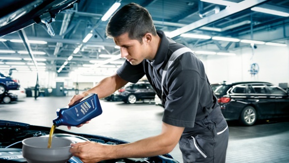 Mechaniker füllt Öl in Auto in heller Werkstatt ein, im Hintergrund weitere Fahrzeuge.