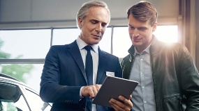 Zwei Männer in Anzügen betrachten ein Tablet in einem BMW Autohaus.