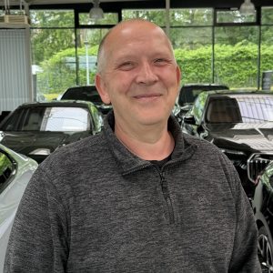 Eine Person in grauem Pullover steht in einem Autohaus vor mehreren schwarzen Autos.