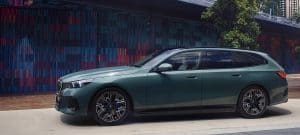 Grünes BMW-Auto vor bunter Wand und Baum im Hintergrund.