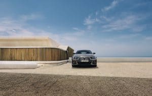 Ein grauer BMW i4 steht vor einem modernen Gebäude unter blauem Himmel.