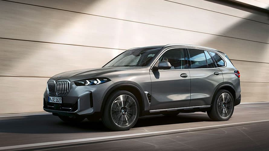 Silberner BMW X5 in Bewegung vor einer beigen Wand.
