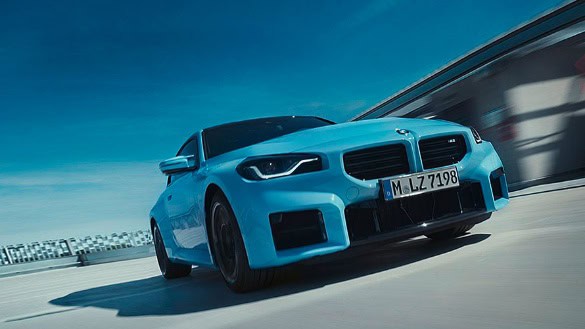 Blaues BMW 2er Coupé auf einer Straße bei Tag, dynamische Perspektive von vorne.