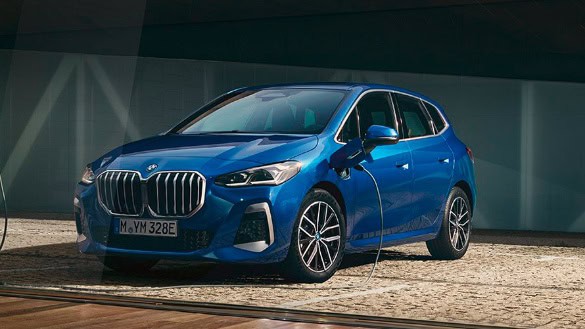 Blauer BMW Plug-in-Hybrid auf gepflastertem Boden, seitlich von vorn, Ladekabel angeschlossen.