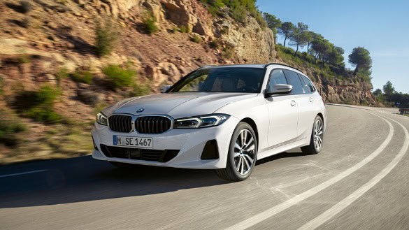 Weißer BMW auf kurviger Straße vor felsiger Landschaft mit Bäumen.