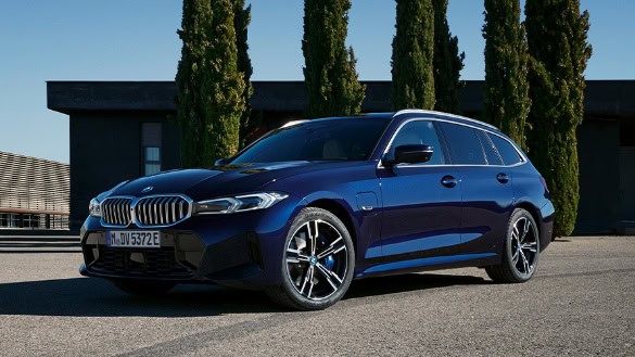 Blauer BMW Kombi vor moderner Gebäude- und Baumkulisse bei sonnigem Wetter.