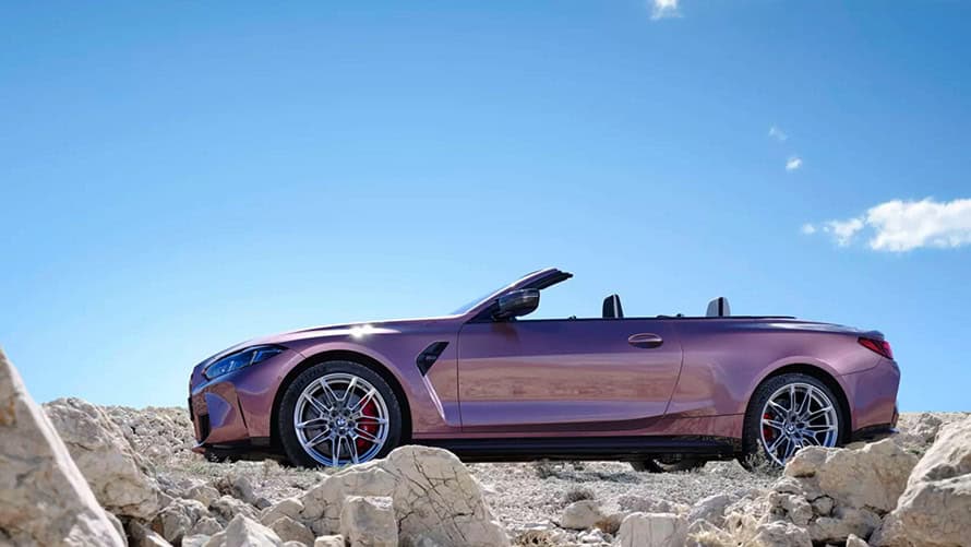 Cabriolet in Metallic-Rot auf felsigem Untergrund, blauer Himmel im Hintergrund.