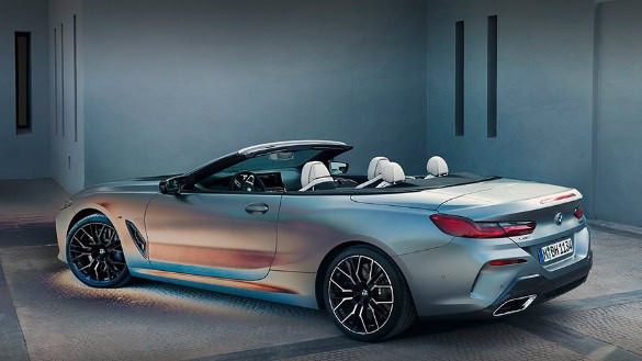 Silbernes BMW-Cabriolet mit offenem Verdeck vor grauer Wand.