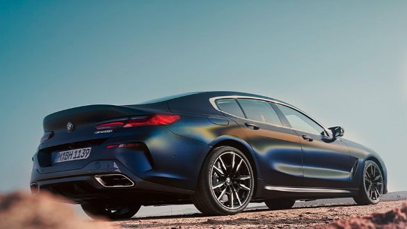 Blaues BMW 8er Gran Coupé auf einer Straße, seitliche Rückansicht, klarer Himmel.