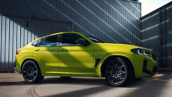 Hellgrüner BMW X4 M steht vor einer metallischen Industriehalle bei Tageslicht.
