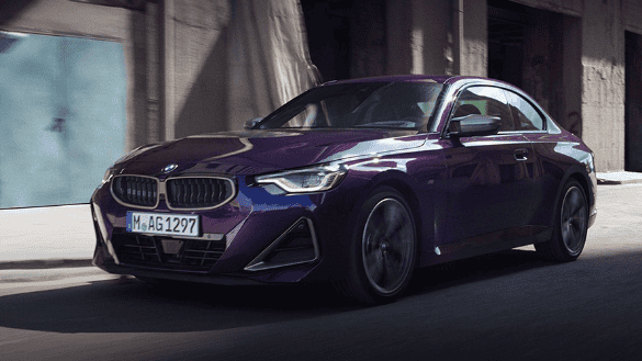 Lila BMW Coupé fährt durch städtische Umgebung, Seitenansicht, sonniges Wetter.