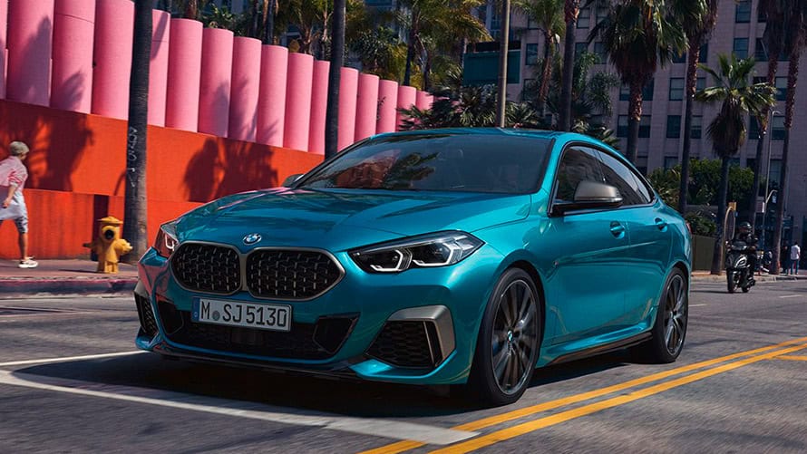 Blaues BMW 2er Coupé fährt auf Straße, im Hintergrund Palmen und rosafarbene Wand.