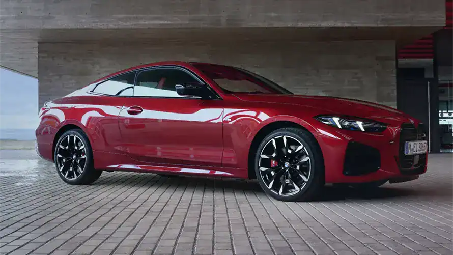 Rotes BMW 4er Coupé, seitlich auf gepflastertem Boden vor Betonwand.