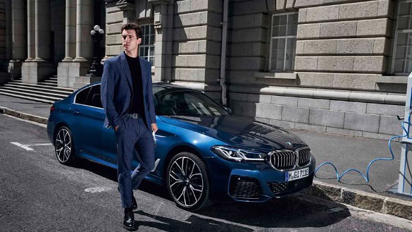 Ein Mann steht neben einem blauen BMW, der an einer Ladestation angeschlossen ist.