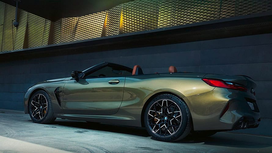 Grünes BMW Cabrio seitlich, geparkt vor moderner Wand, mit offenem Verdeck und schwarzen Felgen.