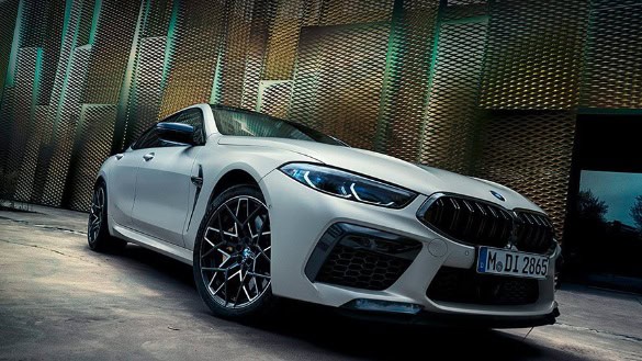 Weißes BMW 8er Coupé vor moderner Metallfassade, schräg von vorne fotografiert.