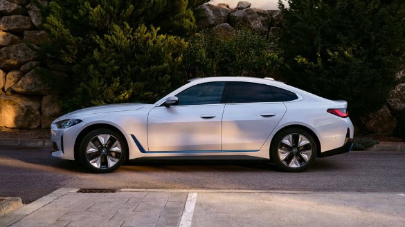 Weißer BMW i4 seitlich auf Straße, im Hintergrund Bäume und Felsen.