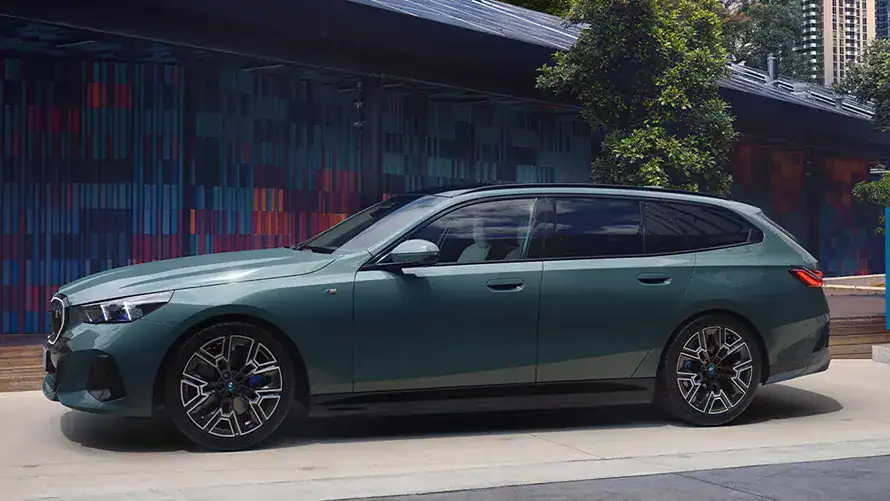 Grüner BMW Kombi vor modernem Gebäude und Bäumen.