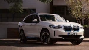 Weißer BMW iX3 SUV ist seitlich im Freien an eine Ladestation angeschlossen.