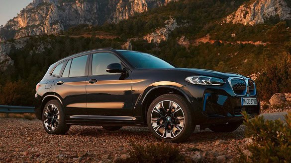 Schwarzer BMW iX3 auf steiniger Straße vor Bergkulisse bei Sonnenuntergang.