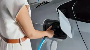 Person lädt ein graues Auto mit einem blauen Kabel an einer Ladestation auf.