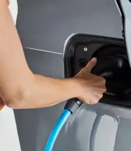 Eine Person lädt ein graues Auto mit einem blauen Ladekabel auf.