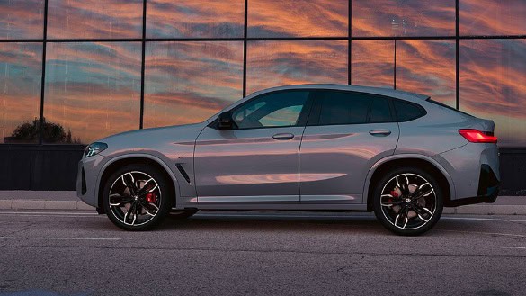 Silberner BMW X4 vor verspiegeltem Gebäude bei Sonnenuntergang.