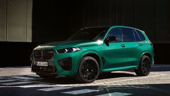Grüner BMW X5M 2023, seitliche Ansicht, geparkt auf gepflastertem Boden, dunkler Hintergrund.