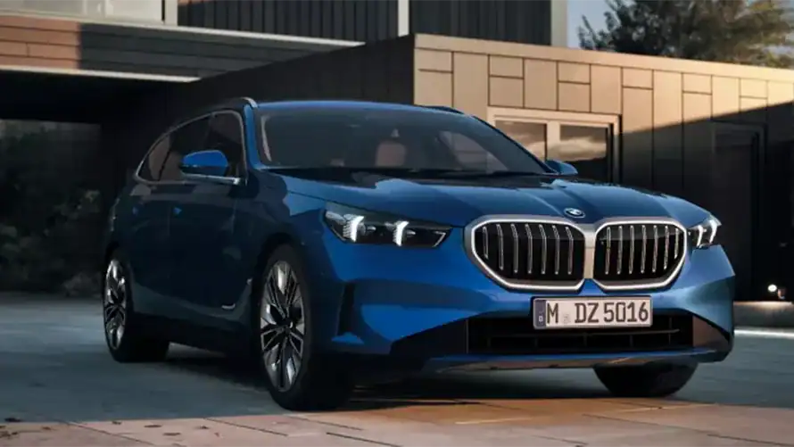 Blauer BMW 5er Touring 2024 vor modernem Gebäude bei Tageslicht.