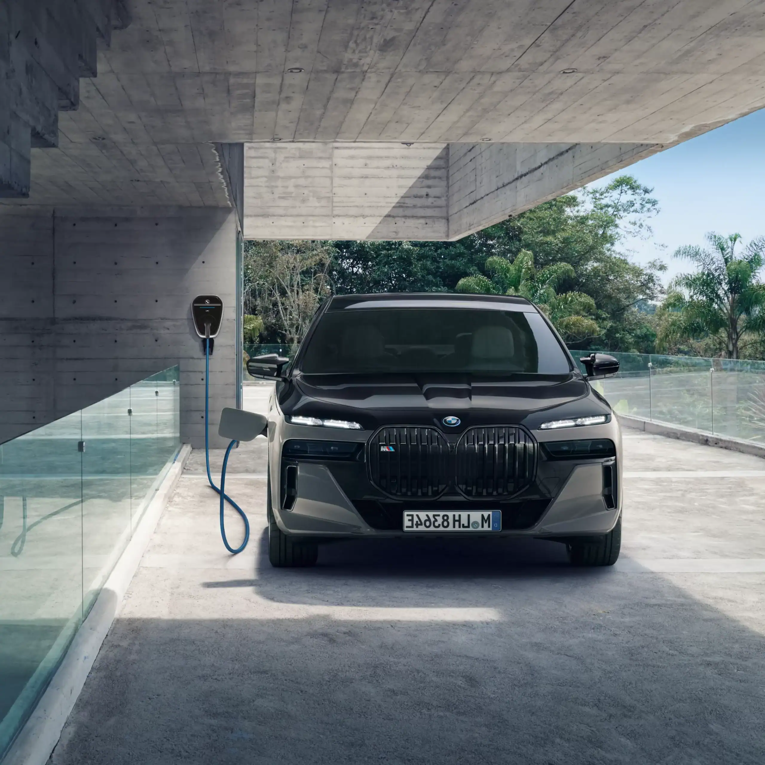 Schwarzer BMW an einer Wallbox in einer modernen Einfahrt, umgeben von Glas und Natur.