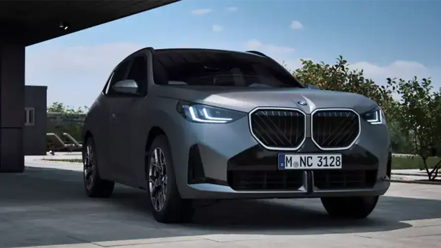 Grauer BMW SUV mit markantem Kühlergrill, parkend auf einer überdachten Fläche bei Tageslicht.
