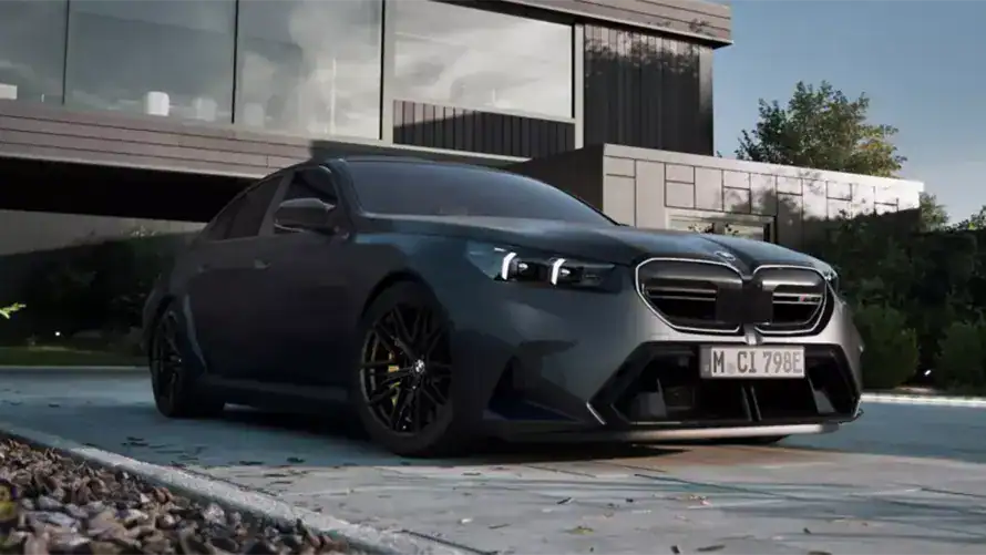 Dunkelgrauer BMW vor modernem Gebäude, sonniger Tag, Bäume im Hintergrund.