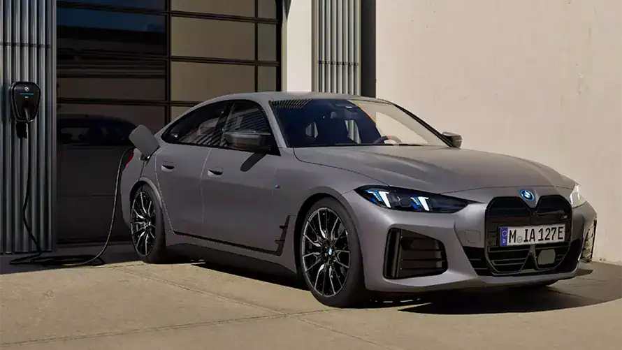 Graues BMW i4 M50 Auto lädt an einer Ladestation vor einem Gebäude.