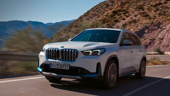 Weißer BMW SUV fährt auf einer Straße in bergiger Landschaft bei Sonnenschein.