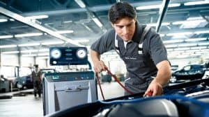 Mechaniker prüft Klimaanlage eines Autos in Werkstatt mit blauem Licht und Diagnosegerät.