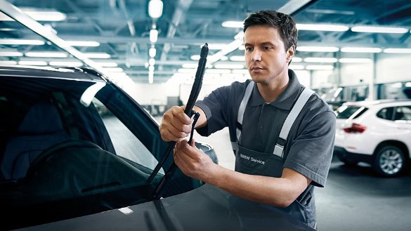 Ein Mann prüft einen Scheibenwischer an einem schwarzen Auto in einer Werkstatt.