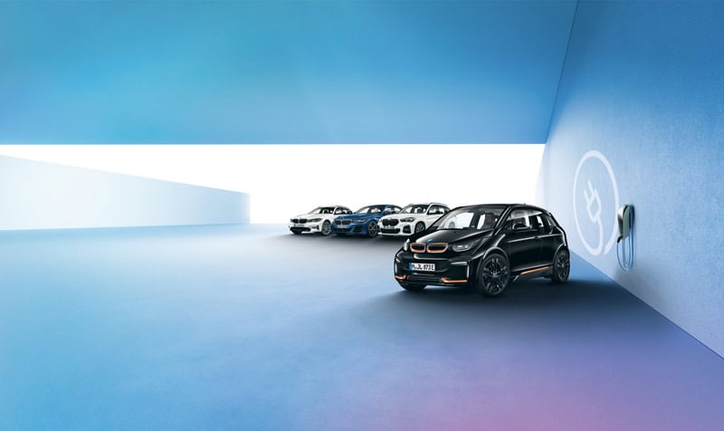 Mehrere BMW-Autos in einer blauen Garage, rechte Wand mit Ladestation.