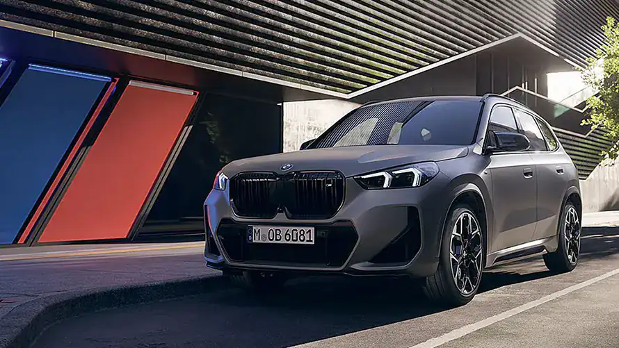 Grauer BMW SUV parkt vor einem modernen Gebäude mit roten und blauen Akzenten.