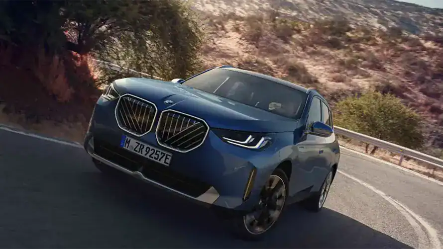 Blauer BMW-SUV auf kurviger Straße in trockener, buschiger Landschaft bei Tageslicht.