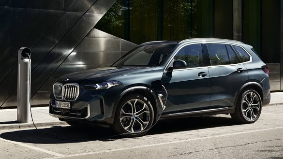 Dunkelblauer BMW X5 an Ladestation vor modernem Gebäude.