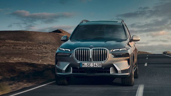 BMW SUV fährt auf einsamer Straße in Landschaft mit Hügeln, unter bewölktem Himmel.