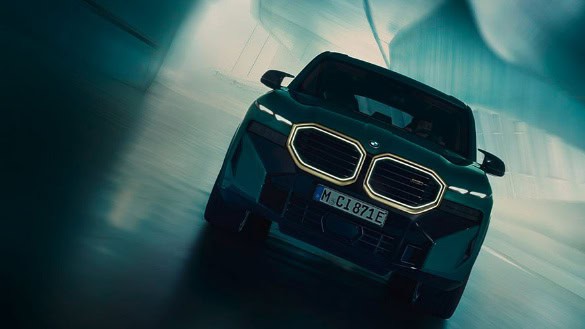 Dunkler BMW mit leuchtendem Nierengrill in futuristischer Umgebung, Vorderansicht.