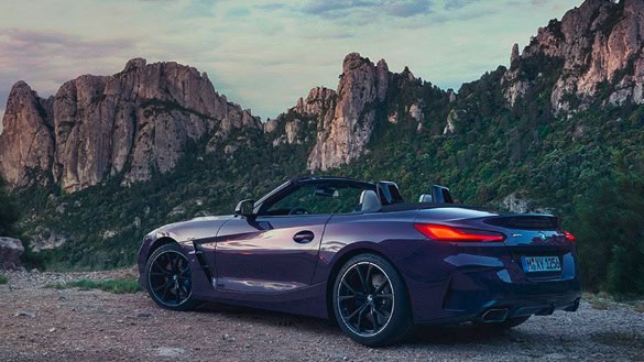 Lila BMW Z4 Roadster vor einer felsigen Berglandschaft bei Sonnenuntergang.