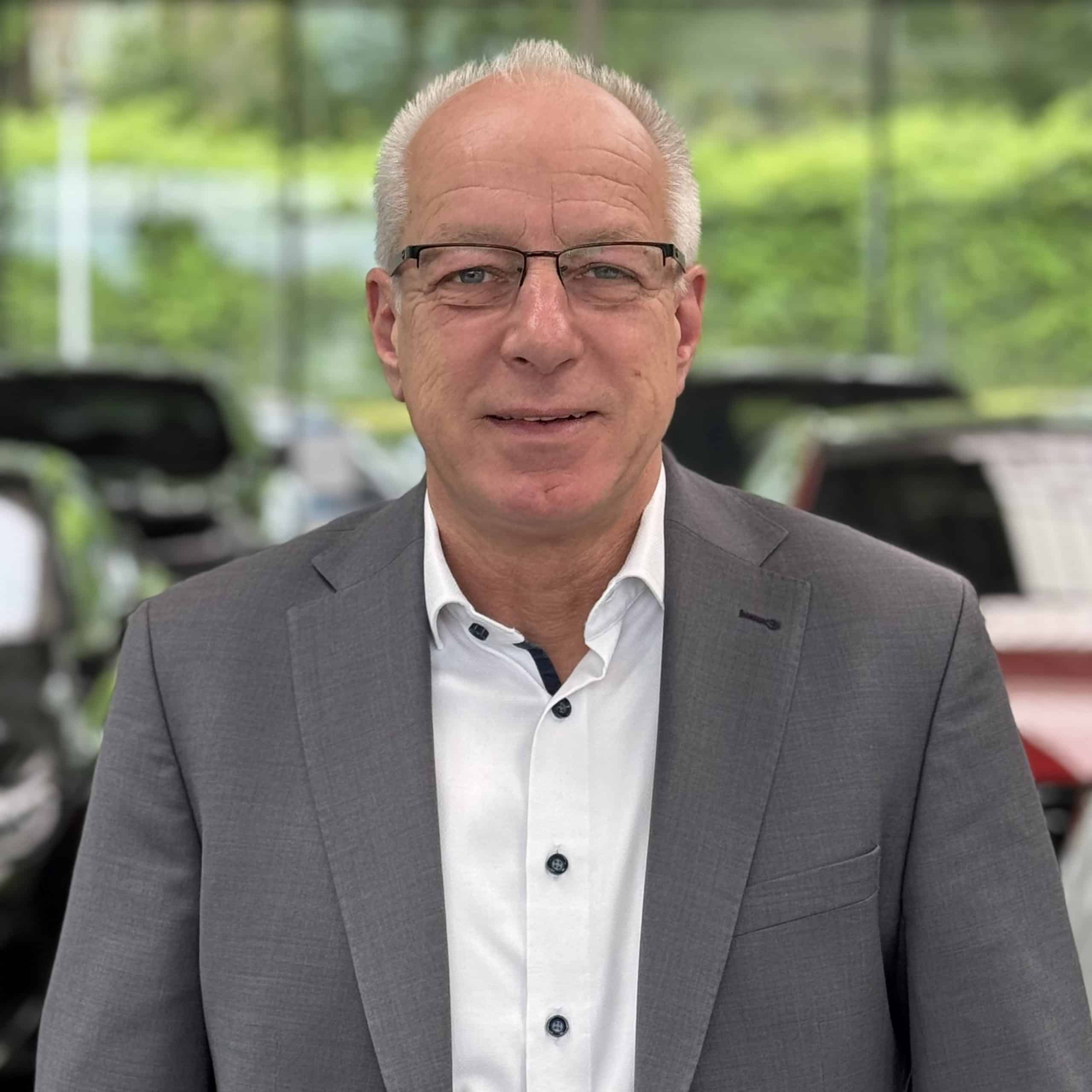 Eine Person im Anzug mit blau gestreifter Krawatte steht vor einem unscharfen Hintergrund.